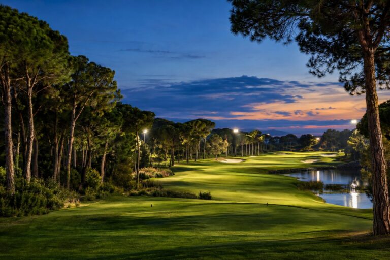 Verlichte fairway tussen pijnbomen op de Carya-golfbaan in Belek bij schemering.